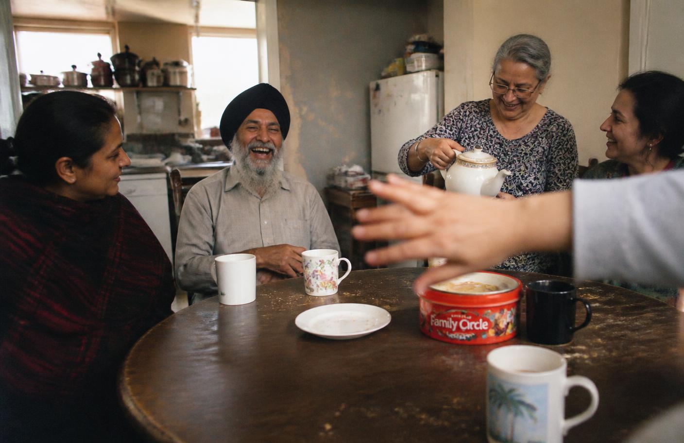 A diverse group of older adults and companions laughing together around a kitchen table